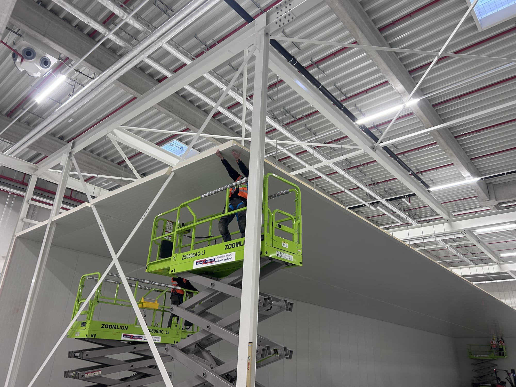 Installers on scissor lifts fixing roof steelwork inside a clad hall